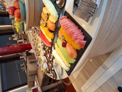       Buffet table laden with sliced tropical fruits and desserts in a cruise dining room.
  