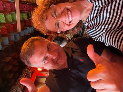       Cheerful close-up selfie of two travelers inside a festive bar.
  