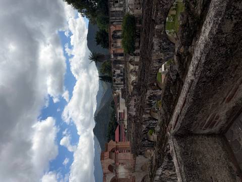       View over colonial ruins with mountain range and dramatic clouds in the background.
  