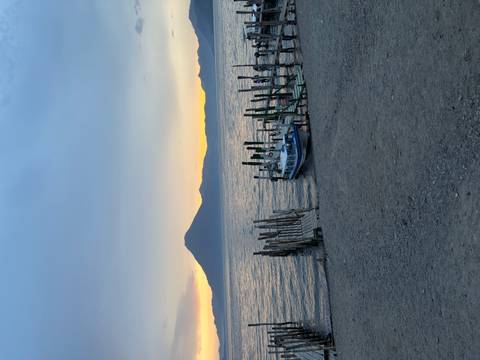       Tranquil lake scene at sunset with a wooden dock, small boat and a volcanic mountain silhouette in the background.
  
