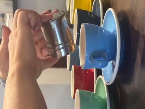       Two people preparing egg coffee, one pouring from a metal filter into a blue cup.
  
