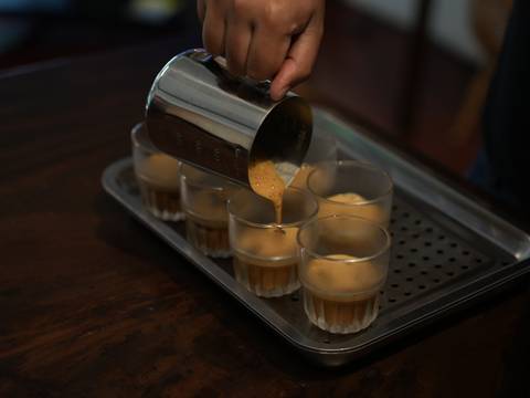      Barista hand pouring espresso into several small glasses arranged on a metal tray.
  