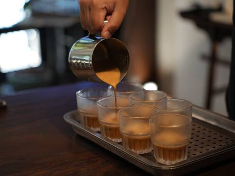       Espresso being smoothly poured from a metal jug into lined-up glasses on a tray.
  