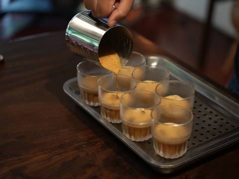       Barista pours thick coffee into eight small glasses placed on a perforated tray.
  