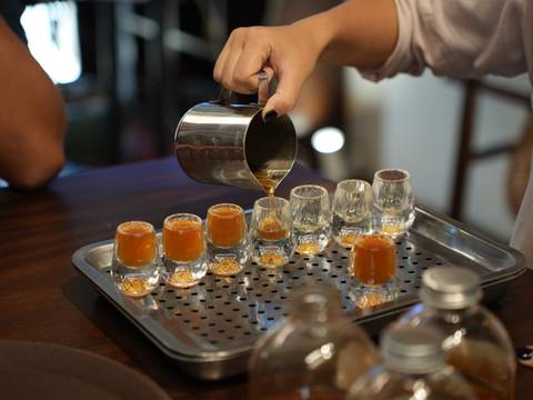       Second angle of barista pouring coffee into clear shot glasses aligned on a metallic tray.
  