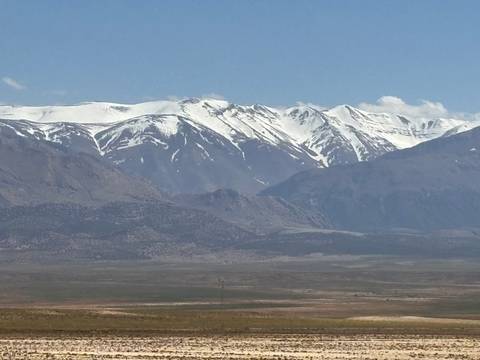       Wide view of the High Atlas range with snow-capped peaks rising above arid foothills and a flat plain.
  