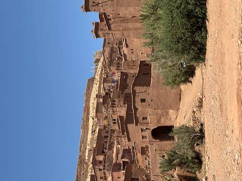       Tall earthen ramparts and towers of a kasbah rise against a flawless blue Moroccan sky.
  