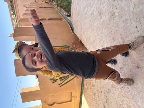       Two playful children pose energetically in a sunlit courtyard with adobe walls and a cactus behind them.
  