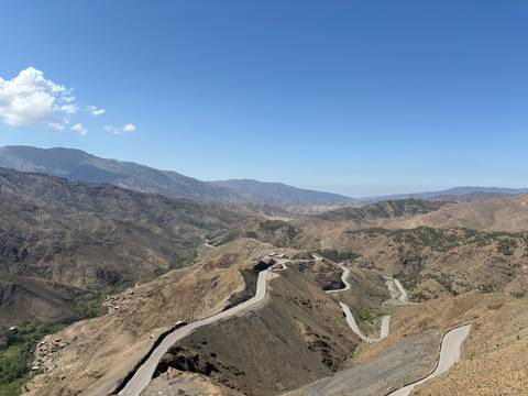       Sweeping view over winding mountain roads cutting through brown ridges of the High Atlas under a clear sky.
  