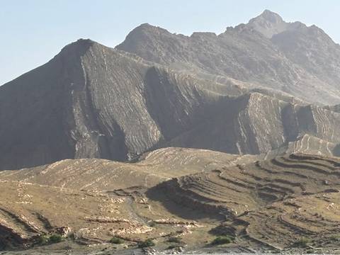       Layered and terraced rock formations on rugged mountain slopes under hazy light.
  