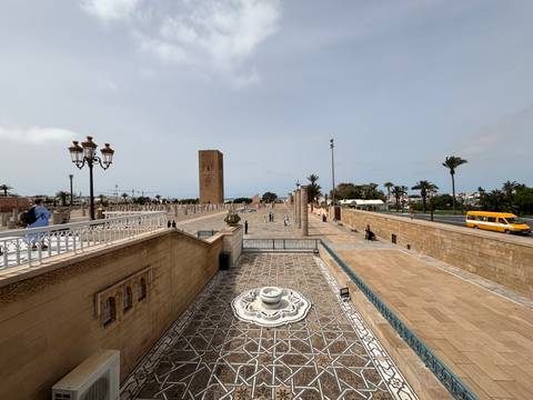       Wide plaza leading to Hassan Tower with fountains, palm-lined avenues and distant visitors exploring.
  
