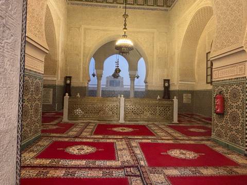       Intricately tiled and carpeted mausoleum interior with ornate arches and chandeliers.
  