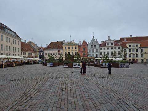      Wide view of Tallinn’s Raekoja plats lined with colourful gabled houses and outdoor cafés.
  