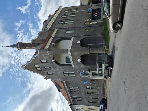       Eclectic grey stone building with blue flags and an arched balcony set beneath a patchy sky.
  