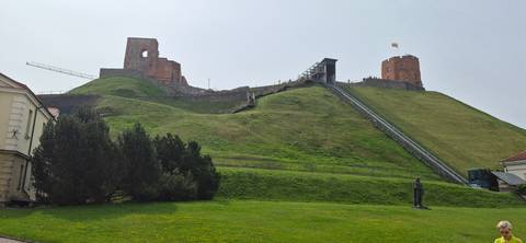       Grassy hill topped by Gediminas Tower and ruins, with a funicular track rising steeply to the summit.
  