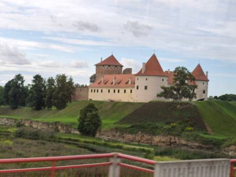       Distant view of a pale castle with orange roofs on a grassy bluff beside a river, but the picture is noticeably unfocused.
  
