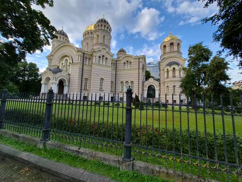       Riga’s Nativity of Christ Cathedral with its gilded domes behind an iron fence and manicured lawn.
  