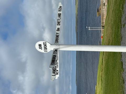       Iconic white signpost at John O'Groats pointing to global destinations with the sea and cloudy sky behind.
  