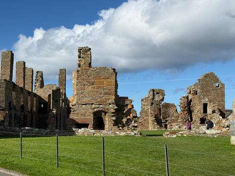       Visitors exploring extensive stone ruins bathed in sunlight against a blue sky with scattered clouds.
  