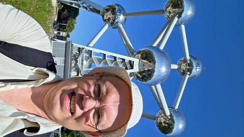       Traveler’s selfie with the gleaming metallic spheres of the Atomium towering behind under clear blue skies.
  