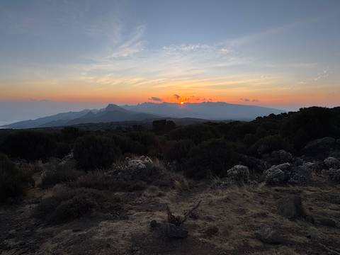       Sunset over layered ridges and scrubland on Kilimanjaro creating a warm horizon glow.
  