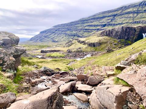       Broad valley with terraced green cliffs, scattered rocks and a small stream winding through the landscape.
  