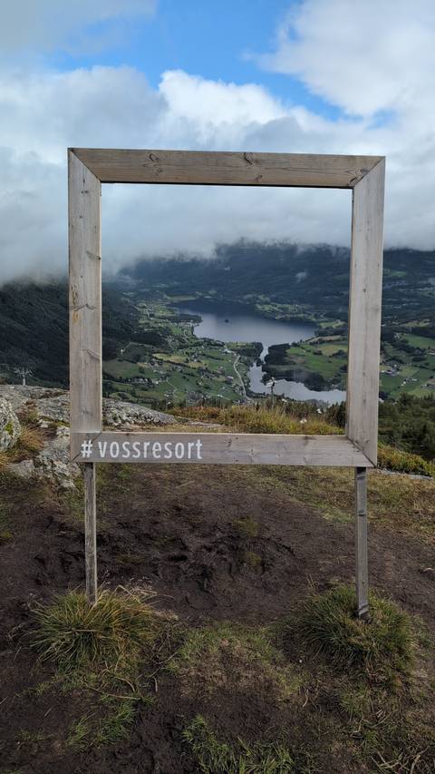       Wooden picture frame labeled #vossresort overlooks a verdant valley, lake, and villages below.
  