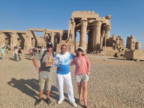       Visitors pose in front of the sandstone columns and hypostyle hall of Kom Ombo Temple under clear Egyptian skies.
  