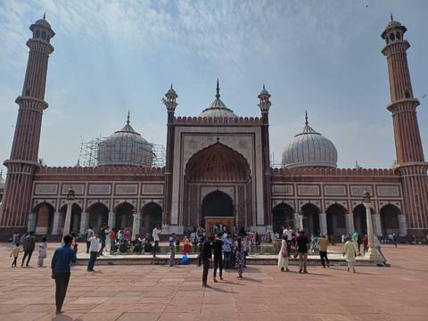       Crowds gather in front of Jama Masjid’s grand marble and red-sandstone façade with towering minarets in Delhi.
  