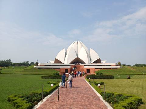       Visitors walk the pathway toward the white-petaled Lotus Temple set amid manicured lawns under blue skies in Delhi.
  