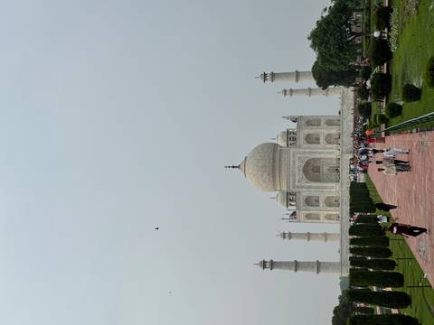       Iconic view of the Taj Mahal framed by gardens and walkways under a hazy sky.
  