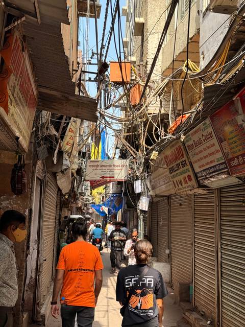       Tangled electrical wires hang above a bustling narrow lane filled with signage and shoppers.
  