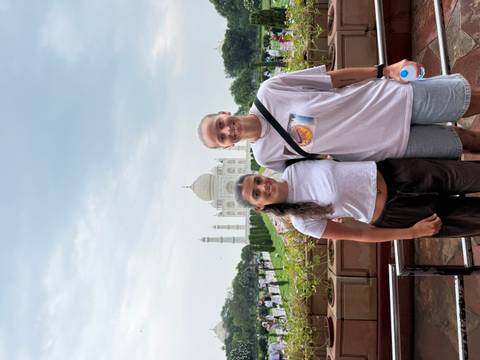       Two travelers pose happily with the Taj Mahal shimmering behind them.
  
