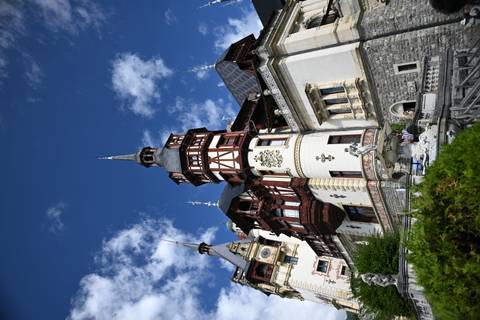       Ornate Peleș Castle with timbered towers and stone façade set against a bright blue sky.
  