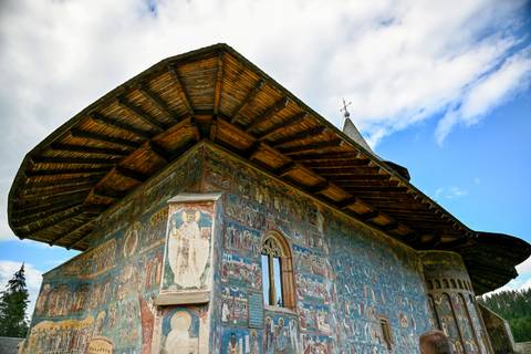       Sucevița Monastery exterior richly decorated with vivid biblical frescoes under a dramatic roof.
  