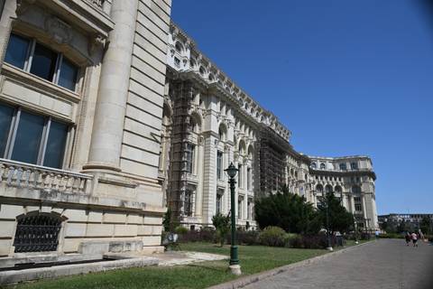       Side view of Romania's massive Palace of Parliament with ornate columns under a clear blue sky.
  