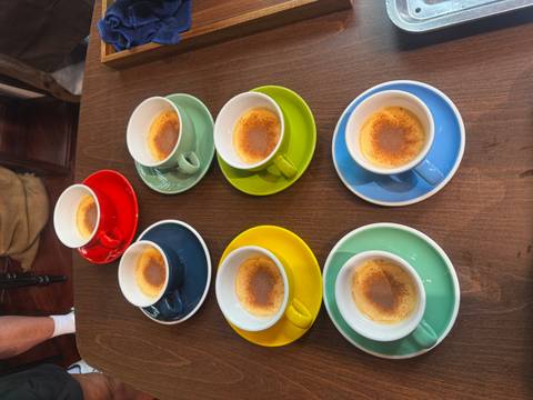       Six colorful espresso cups filled with Vietnamese egg coffee arranged on a wooden table.
  