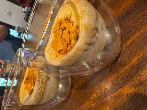       Two double-walled glasses of egg coffee topped with crispy flakes on wooden counter.
  