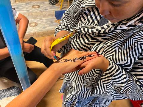       Artist applies intricate black henna design to a visitor's hand.
  