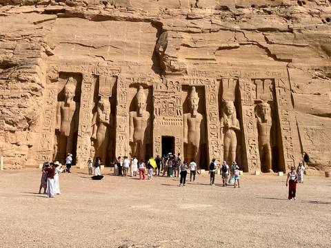       Crowds explore the grand rock-hewn façade of Abu Simbel temple under bright sun.
  