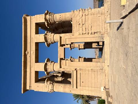       Stone gateway with towering lotus-flower capitals at Philae Temple framed by blue sky and water beyond.
  