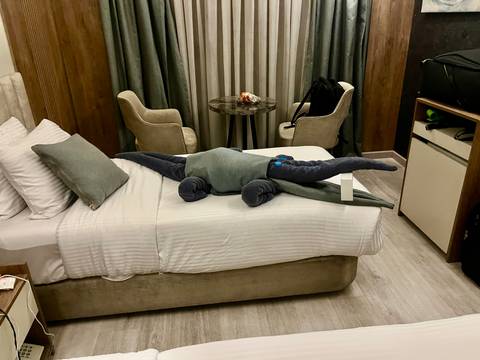       Hotel room bed decorated with a towel folded into a crocodile shape, luggage nearby.
  