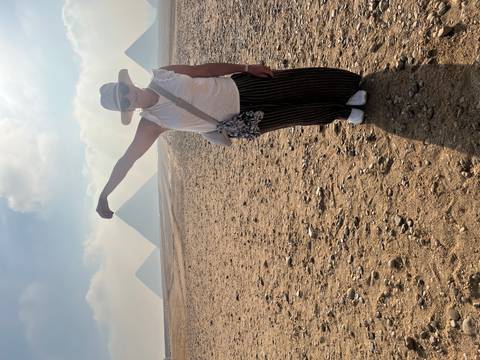       Traveler jokingly 'pinches' distant pyramids while standing on a sandy plain in Giza.
  