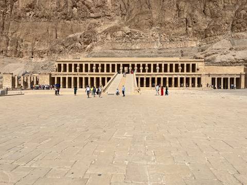       Wide plaza leading to Queen Hatshepsut's terraced mortuary temple with visitors scattered around.
  