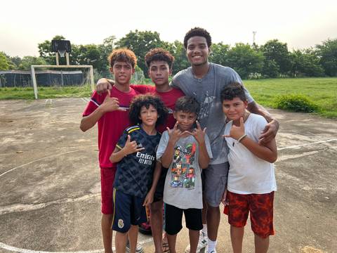       Youthful team poses on an outdoor basketball court with greenery and goals behind.
  