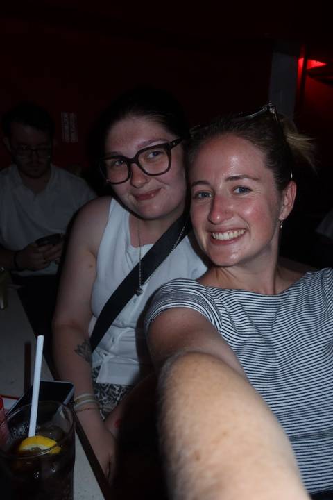       Two young women take a flash selfie in a dimly lit indoor setting.
  