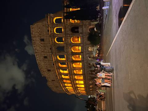       The Colosseum dramatically lit at night with visitors gathering around the monument.
  
