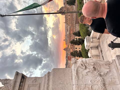       Sunset view over Rome rooftops and St Peter’s dome framed by dramatic clouds.
  