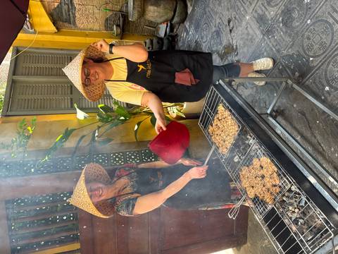       Two women in conical hats grilling meat over charcoal during Vietnamese cooking class
  