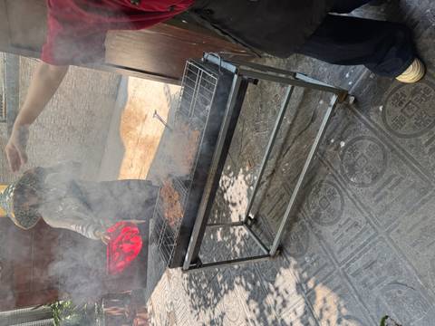       Smoky outdoor charcoal grill with patties and person fanning flames
  